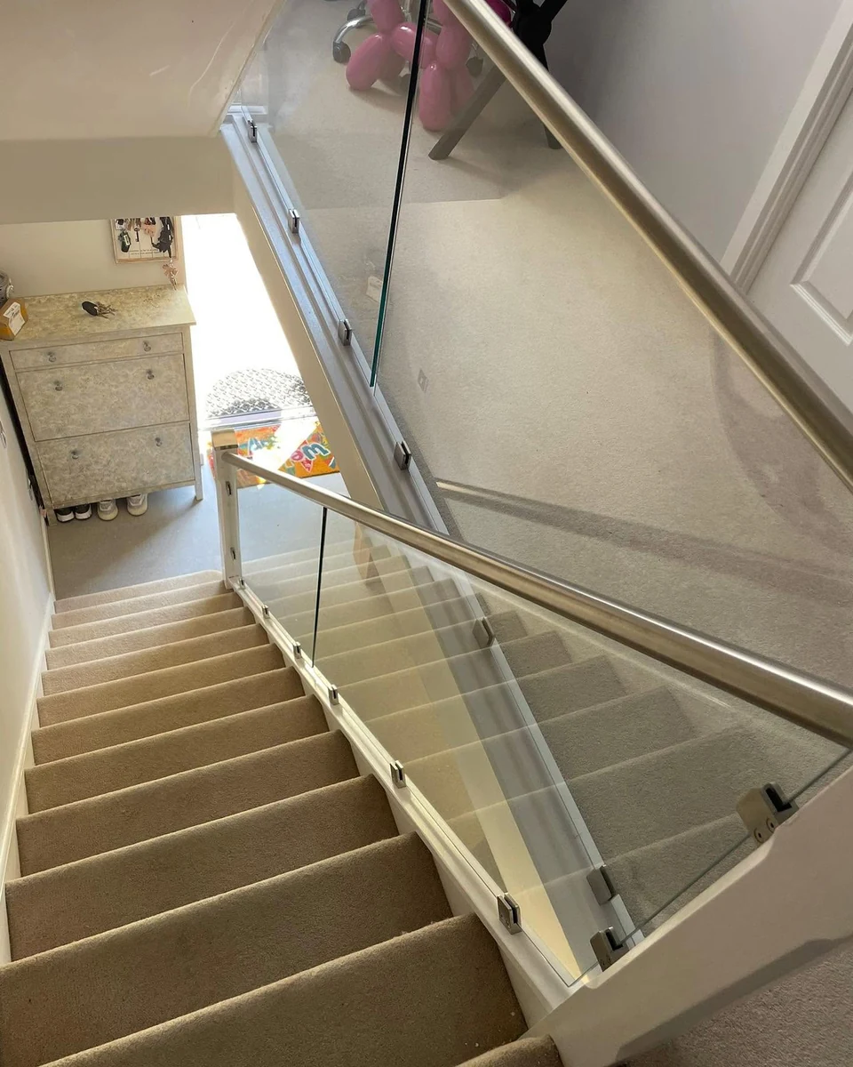 staircase-glass-balustrade-steel-handrail-downview-sevenoaks-sevenoaks-glass-balustrades Frameless glass balustrade with stainless steel handrail viewed downward from landing, Sevenoaks